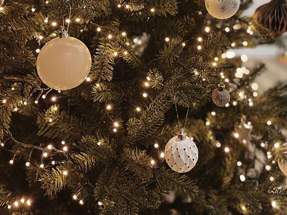 Christmas tree branches with glowing lights and neutral-toned ornaments.