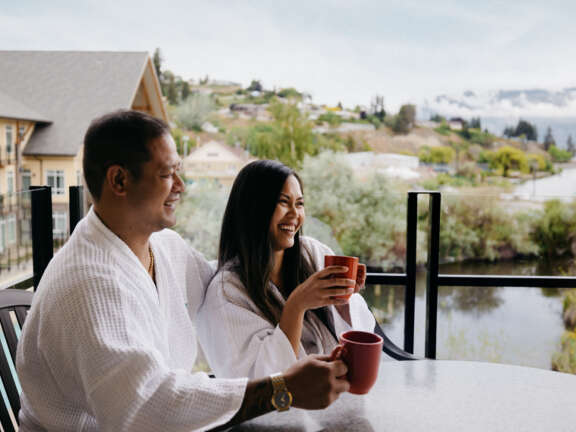Summerland Waterfront Resort & Spa Gift Certificates - couple smiling and enjoying coffee on the balcony overlooking the lake.